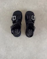 Sandalias negras de cuero sintético con plataforma y hebillas plateadas.
