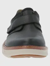 Zapato de cuero negro con ajuste de velcro, punta redonda y suela de goma color crema.