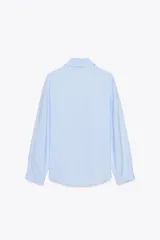 Camisa celeste de cuello solapa y manga larga con pliegues. Bajo asimétrico y cierre frontal con botones.