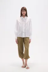 Camisa blanca de broderie con cuello camisero, cierre frontal de botones, mangas largas y corte holgado.