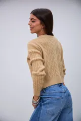 Sweater de punto color beige con cuello redondo, mangas largas y detalles de trenzas en el frente y las mangas.