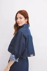 Camisa de denim azul con cuello clásico, cierre frontal con botones, mangas largas con puños abotonados y dos bolsillos tipo cargo en el pecho.