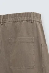 Pantalón cargo de algodón color marrón con efecto lavado, corte relajado y tiro medio. Presenta cintura elástica con botón y cierre de cremallera, bolsillos delanteros, bolsillos plastrón en la espalda y grandes bolsillos cargo en las perneras.