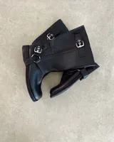 Bota de caña media de cuero negro con hebillas metálicas plateadas decorativas en la caña y alrededor del tobillo.