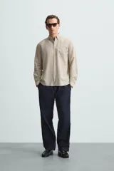 Camisa celeste a rayas verticales, de corte relaxed fit, confeccionada en lino y algodón. Tiene cuello abotonado, manga larga con puños abotonados, bolsillo de parche en el pecho y cierre frontal con botones.