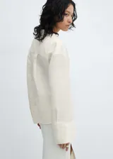 Blusa color crudo de lino con diseño cruzado y cierre con botones. Tiene cuello camisero, manga larga y bajo asimétrico.