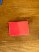 Tarjetero azul de cuero charol con tres ranuras para tarjetas y logo de la marca grabado en una placa dorada.