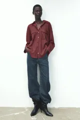 Camisa color borgoña a rayas verticales finas, de corte recto, con cuello solapa y manga larga. Tiene dos bolsillos de parche con solapa en el pecho y cierre frontal con botones.