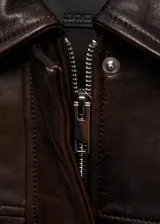 Chaqueta bomber de cuero color marrón oscuro con cuello camisero y cierre frontal con cremallera y botones a presión. Tiene terminaciones elásticas en puños y cintura, y dos bolsillos laterales.