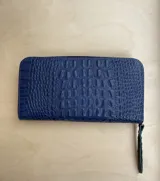 Billetera de cuero color verde pistacho con cierre perimetral y logo metálico de la marca en el frente.