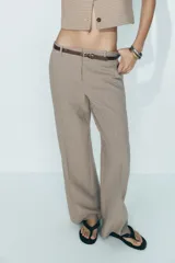 Pantalón de tiro alto con estampado a cuadros en tonos beige y marrón, con bolsillos delanteros y falsos bolsillos traseros. Incluye cinturón marrón con hebilla metálica.