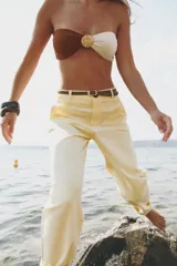 Pantalón chino color amarillo claro, de tiro medio, con bolsillos frontales y traseros. Incluye cinturón trenzado marrón.