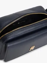 Cartera tipo cámara estructurada de color azul marino, con solapa frontal y logo metálico de Tommy Hilfiger en dorado. Posee un bolsillo externo con cierre de solapa a broche y correa ajustable extraíble.