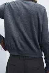 Chaqueta de punto fino color gris oscuro confeccionada con lana. Tiene cuello redondo, manga larga y cierre frontal con botones.