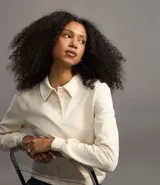 Suéter de manga larga color crema, con cuello polo y tapeta de botones.