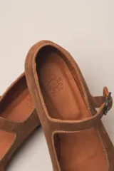 Zapato estilo Mary Jane color marrón, de cuero, con punta redondeada y tira sobre el empeine con hebilla.