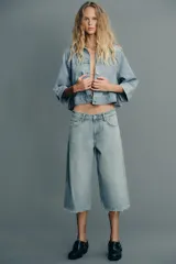 Cazadora de denim celeste con cuello solapa y manga tres cuartos. Cierre frontal con botones metálicos.