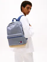 Mochila Tommy Jeans Essential con diseño a rayas verticales azules y blancas, base color beige, asa superior y correas acolchadas ajustables. Cuenta con compartimento principal con cierre de cremallera, bolsillo interior de malla y bolsillo exterior con cremallera.
