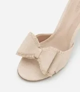 Sandalia color beige con capellada de rafia, taco fino y maxi lazo decorativo.