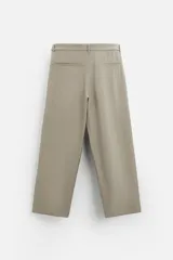 Pantalón negro de corte amplio, con pliegues frontales, bolsillos laterales y traseros de ojal. Incluye cinturón de la misma tela con hebilla metálica.
