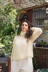 Sweater tejido a mano en lana merino color crema, con cuello alto tipo polerón y mangas largas.