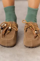 Zueco de cuero gamuzado color beige, con cordones decorativos con cuentas y piezas envueltas en cuero. Tiene plantilla acolchada y base liviana.