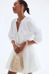 Blusa blanca de popelina de algodón con cuello mao, abertura en V y botones frontales. Mangas globo tres cuartos de corte raglán con puños finos y bajo recto.