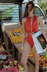 Body de una pieza color rojo vibrante con textura sutil, escote profundo pronunciado y tirantes finos que se anudan en el centro del pecho. Presenta recortes laterales (cut-out) y espalda descubierta.