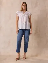 Blusa color marrón claro de algodón con bordados y calados blancos. Tiene cuello a la base, escote en V con lazo de ajuste y mangas cortas amplias.