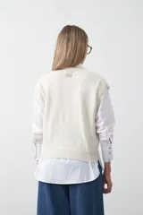 Chaleco de punto color blanco con bordado aplicado de cordón marrón en diseño floral. Presenta cierre frontal de botones al tono, cuello redondo y terminaciones acanaladas en sisas y ruedo.