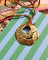 Collar con cordón naranja y dije de flor dorada.