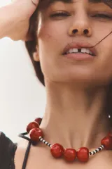 Collar corto con cuentas pequeñas blancas y negras, y dijes grandes de cerezas rojas. Cierre de mosquetón dorado.