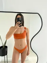 Conjunto de bikini color naranja, con corpiño de un solo hombro con aro metálico y bombacha colaless.