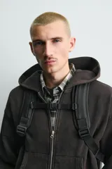 Mochila negra con acabado engomado, múltiples bolsillos frontales de diferentes tamaños con cierre de cremallera e imán, bolsillos laterales, parte posterior acolchada con banda de sujeción para equipaje, asa de mano y dos asas de hombro ajustables y acolchadas.