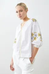 Blusa blanca de estilo boho con bordados de flores en amarillo y azul en mangas y escote.