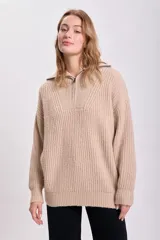 Sweater beige de punto grueso, con cuello polo y cierre metálico parcial.