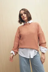 Sweater de punto color salmón con cuello redondo y mangas anchas. Presenta un diseño calado en la parte superior y tejido tramado horizontal en el resto del cuerpo.