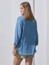 Camisa celeste de tencel con cuello con solapa, escote en V, abertura central con botones, bolsillo aplicado en el frente y ruedo desflecado.