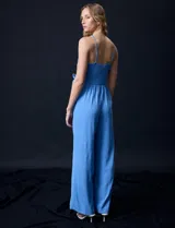 Enterito celeste de crepe marca Luxology, con escote en V cruzado, cintura elastizada, espalda en punto smock y tirantes con detalle de cadenas.