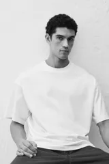 Remera blanca de algodón de peso medio, con cuello redondo ribeteado, hombros caídos y bajo recto. Corte oversized.