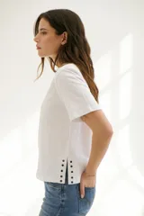 Remera blanca de algodón de corte recto, con cuello redondo y mangas cortas. Presenta detalle de aberturas laterales con ojales metálicos.