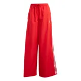 Pantalón Adidas rojo de corte ancho con cintura elastizada y cordón ajustable. Presenta las tres tiras blancas características de la marca en los laterales y el logo bordado en la pierna izquierda.