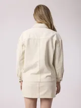 Campera de jean color beige, de corte recto, con cuello clásico, cierre frontal con botones metálicos, bolsillos de parche en el pecho y mangas largas con puños abotonados.