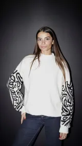 Sweater de punto color crudo con cuello alto y bordado de arabescos negros en las mangas. Corte holgado.