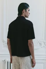 Camisa de manga corta negra con textura, cuello abierto, tapeta lisa y bajo recto.