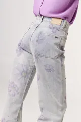 Pantalón de jean celeste con estampado de flores color lila.