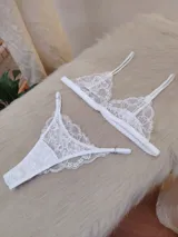 Conjunto de lencería blanco de encaje, compuesto por un bralette triangular con breteles regulables y una tanga regulable de corte less con entrepierna de algodón.