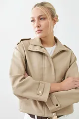 Chaqueta corta color beige de cuero sintético, con cuello alto, cierre frontal con botones a presión y bolsillos laterales con solapa.