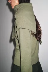 Chaqueta de punto color rosa pálido, con cuello redondo y cierre frontal de botones oscuros. Presenta mangas largas y un corte a la cintura.