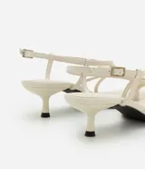 Sandalia femenina confeccionada en material sintético color crema, con punta redonda, tiras finas asimétricas, dedera con detalle bold y hebilla lateral. Prenda con salto mediano fino.